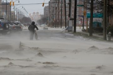Photo:  A man walks down a street covered in beach sand due to flooding from Hurricane Sandy in Long Beach, New York